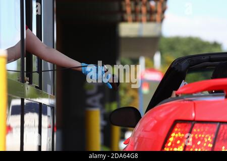 Hand in Schutzhandschuh hält Zahlungsterminal und reicht es Zum Fahrer im Auto Stockfoto