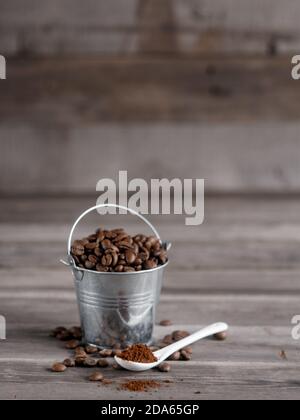 Arabica-Kaffeebohnen in einem kleinen kleinen kleinen Eimer. Gemahlener Kaffee in einem weißen Keramiklöffel auf Holzgrund Stockfoto