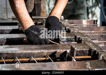 Nahaufnahme eines arbeitenden Mannes in Handschuhen mit Draht bindet die Stange in der Produktion. Der männliche Arbeiter kontrolliert den Produktionsprozess in der Fabrik Stockfoto