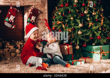 Bruder und Schwester sitzen mit Schachteln in grüner Verpackung mit Geschenken und einem Bogen. Weihnachtsstimmung. Kinder in Neujahrskostümen warten auf ein Stockfoto