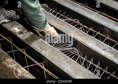 Nahaufnahme eines Arbeiters in Handschuhen dehnt die Stange an der Produktionsstätte aus. Der männliche Arbeiter kontrolliert den Produktionsprozess in der Fabrik Stockfoto