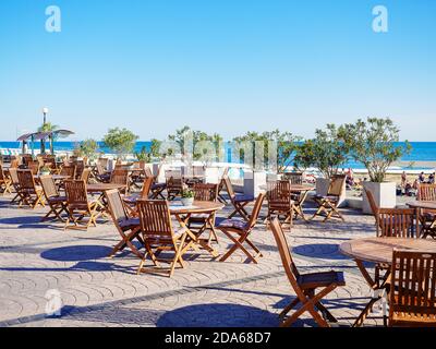 Russland, Sotschi 07.06.2020. Straßencafé mit runden Holztischen und Stühlen auf einer Plattform mit Blick auf das Meer Stockfoto