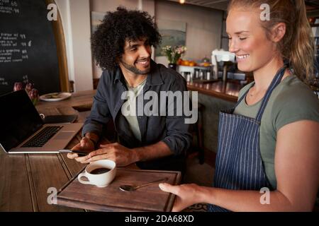 Schöne junge Kellnerin serviert Mann mit lockigen Haaren mit Kaffee Auf dem Tisch Stockfoto