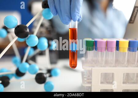 Hand in Handschuh hält Reagenzglas mit Flüssigkeit auf dem Hintergrund Von Molekülen und Reagenzgläsern Stockfoto