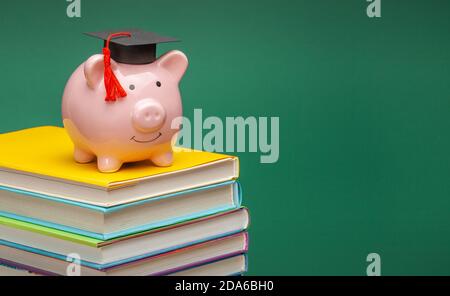 Sparschwein in einem Abschlusshut auf Stapel von Büchern. Grüner Hintergrund. Platz für Text kopieren. Stockfoto