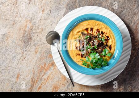 Kürbissuppe mit Wildpilzbrühe, garniert mit Sesamsamen, Winter-beruhigendes Gericht, serviert auf einer blauen Schüssel auf hellem Steingrund, Draufsicht, Stockfoto