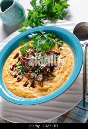 Cremige Kürbissuppe mit Wildpilzbrühe und Kokosmilch Garniert mit Sesamsamen und frischer Petersilie serviert auf einem Blaue Schüssel mit Sojasauce auf einem li Stockfoto