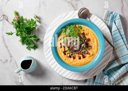 Cremige Kürbissuppe mit Wildpilzbrühe und Kokosmilch Garniert mit Sesamsamen und frischer Petersilie serviert auf einem Blaue Schüssel mit Sojasauce auf einem li Stockfoto