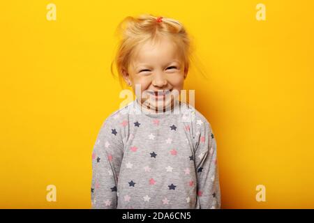 Kind im Pyjama macht Gesichter auf gelbem Hintergrund. Stockfoto