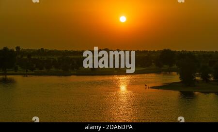 Ein wunderschöner, strahlend orangefarbener Sonnenuntergang und eine wunderschöne Reflexion auf dem ruhigen Wasser des Sees an den Al Qudra Seen in Dubai, Vereinigte Arabische Emirate. Stockfoto