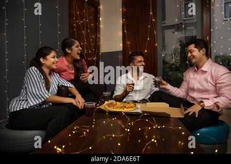 EINE GRUPPE VON BÜROFREUNDEN LACHT UND FEIERT ZUSAMMEN MIT PIZZA UND GETRÄNKE Stockfoto