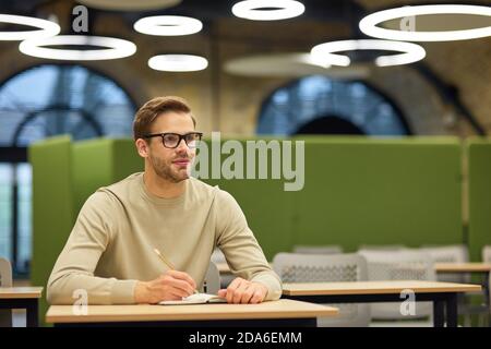 Kaukasischer Mann, männlicher Büroangestellter, der am Schreibtisch im Coworking Space sitzt und sich während des Corporate Trainings oder Seminars Notizen macht. Business Education Konzept Stockfoto