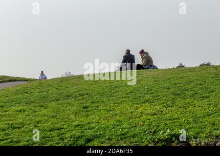 Zwei Männer sitzen auf dem Gras und genießen die Wintersonne auf den Klippen nahe dem Commodore Public House über dem Strand bei Fisherman’s Walk in Boscombe, einem Abschnitt des berühmten sieben Meilen langen Sandstrandes in Bournemouth und Poole in Dorset. 07. November 2020. Foto: Neil Turner Stockfoto