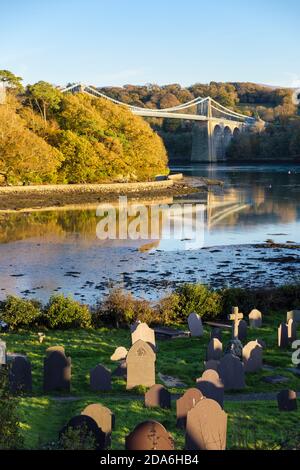 Grabsteine im Kirchhof von St Tysilio auf der Kirchinsel in der Menai-Straße im Herbst mit Menai-Hängebrücke. Menai Bridge Isle of Anglesey Wales Großbritannien Stockfoto