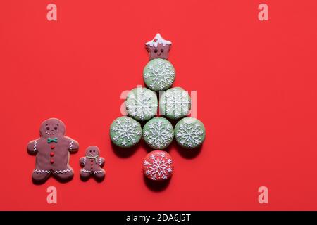 Weihnachtsbaum aus verzierten Makronen Makronen mit Lebkuchen Mann Keksfamilie, die daneben auf rotem Hintergrund steht Mit Kopierbereich Stockfoto