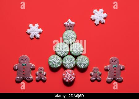 Weihnachtsbaum aus verzierten Makronen Makronen mit Lebkuchen Mann Keksfamilie, die daneben auf rotem Hintergrund steht Mit Kopierbereich Stockfoto