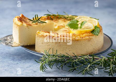 Käsekuchen mit Zitronenvanille, verziert mit Rosmarin-, Minze- und Zitronenscheiben. Ricotta keine Kruste Käsekuchen oder Kasserolle. Blauer Hintergrund. Stockfoto