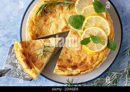 Käsekuchen mit Zitronenvanille, verziert mit Rosmarin-, Minze- und Zitronenscheiben. Ricotta keine Kruste Käsekuchen oder Kasserolle. Blauer Hintergrund. Draufsicht. Stockfoto