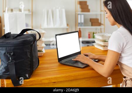 Frau Lebensmittelzustellung Arbeiter in Schürze sitzen Kommunikation online mit Kunde Stockfoto