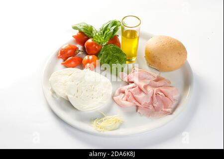 Gericht mit Zutaten für ein Sandwich mit Mozzarella, gekochtem Schinken, Kirschtomate, Basilikum und Öl auf weißem Hintergrund auszuschneiden Stockfoto