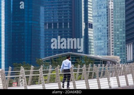 Die ganze Rückenansicht des Büroangestellten trägt eine schwarze Maske und läuft auf der Brücke in einer Geschäftsvierteln-Stadt, Singapur. Stockfoto