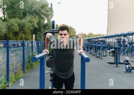 Starker muskulöser junger Mann arbeitet im Fitnessstudio im Freien. Nahaufnahme eines jungen starken Teenagers, der an der horizontalen Stange Pull-up macht. Stockfoto