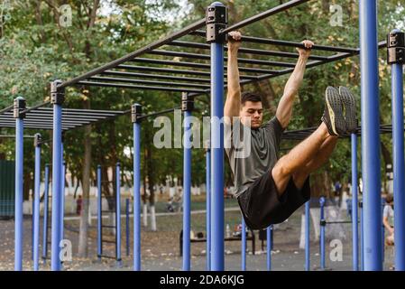 Aufnahme eines jungen Mannes, der Dips auf den unebenen Balken macht. Ein Mann zieht sich an einer horizontalen Stange hoch und hebt seine Beine an Gewicht. Sit-up. Stockfoto