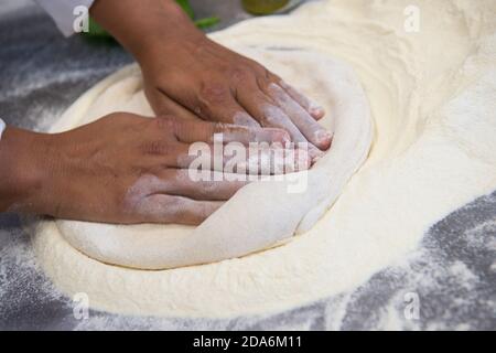 Detail der Hände eines Pizzakochs, der für die verschiedenen Phasen der Vorbereitung einer echten italienischen Pizza hausgemachte mit Hefemehl und Wasser arbeitet. Stockfoto