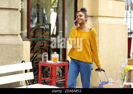 Porträt einer glücklichen jungen afrikanischen Frau mit Reisetasche reden Auf dem Handy auf der Stadtstraße Stockfoto