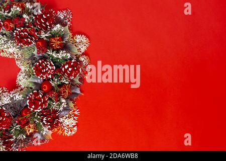 Postkarte eines halben Weihnachtskranzes aus Fichtenzweigen, Flechten, mit Zapfen und Beeren, isoliert auf rotem Hintergrund Stockfoto