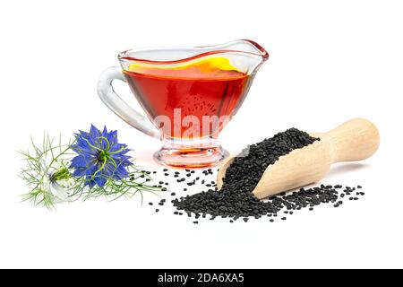 Schwarzes Kreuzkümmelöl in Soße Boot und Nigella Blumen. Nigella sativa Samen in Holzlöffel isoliert auf weißem Hintergrund. Stockfoto