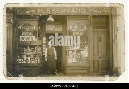 Originalpostkarte aus der Zeit WW1 des Lebensmittelladens mit vielen bekannten Markennamen im Schaufenster mit Anzeigen: Rowntree's, Rinso, Lyons Tea, Brooke Bonds Tea, Bovril, Bird's Spongie (Kuchenmischung) Blue Band Margarine, HP Sauce und Quaker Oats - der Eigentümer ist H. Sheppard, ca. 1917, 1918, Erdington, Birmingham, England, Großbritannien Stockfoto