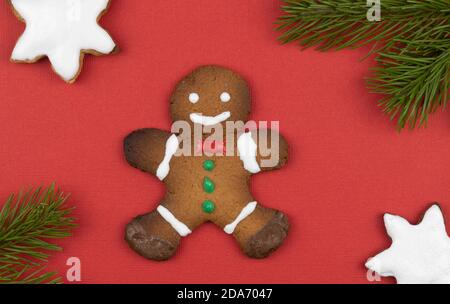 Lebkuchenmänner auf rotem Hintergrund mit Fichtenzweigen verziert. Traditionelle Weihnachten Lebkuchenkekse. Urlaub Leckereien handgefertigt. Stockfoto