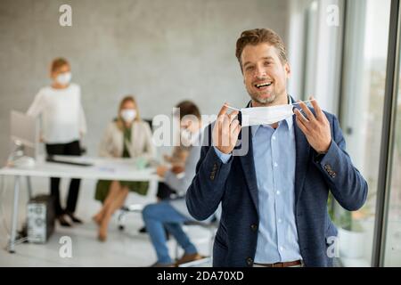 Hübscher junger Geschäftsmann, der seine schützende Gesichtsmaske in die Haut setzt Die Büroflächen Stockfoto