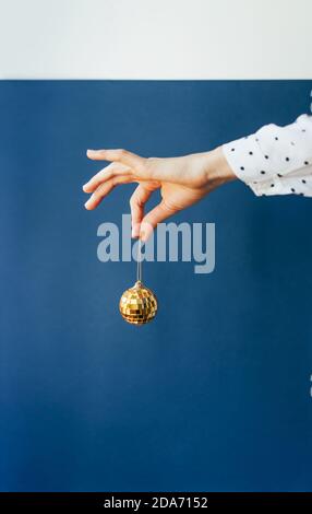 Eine weibliche Hand hält eine goldene Weihnachtskugel Dekoration durch einen Faden. Stockfoto