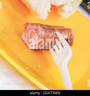 Gegrillte Wurst auf einer Gabel und Brot auf einem gelben Kunststoffplatte Stockfoto