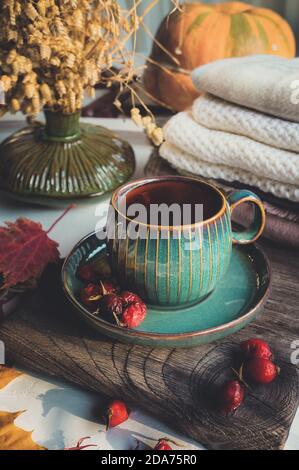 Tasse Tee oder Kaffee mit einer Teekanne in einem herbstlichen Stillleben. Schöne Tasse und Untertasse auf einem Holzbrett umgeben von Herbstblättern, auf dem Hintergrund Stockfoto