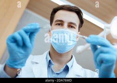 Junge attraktive Zahnarzt in weißem Mantel, Schutzmaske und Gummihandschuhe behandelt Zähne zum Patienten Stockfoto