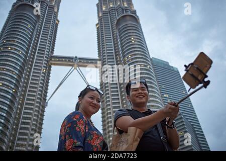 Kuala Lumpur, Malaysia, Februar 2016. Ein Paar macht ein Selfie mit den Petronas Türmen hinter ihnen. Stockfoto