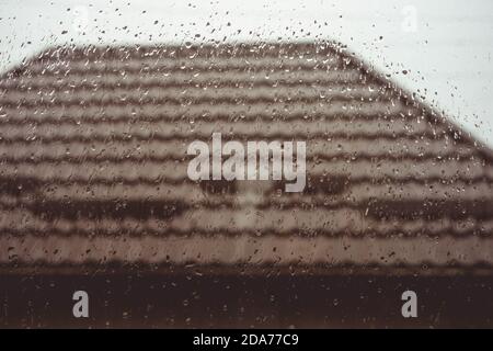 Braun gefliestes Dach vor dem Fenster in Regentropfen. Stockfoto