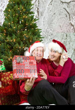 Reifes Paar mit Geschenken unter Weihnachtsbaum in verschneiten Wald-Szene. Stockfoto