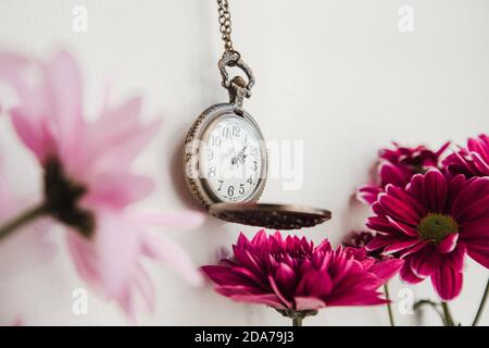 Alte runde Vintage-Uhr auf einer Kette zwischen Blumen in Der Innenraum Stockfoto