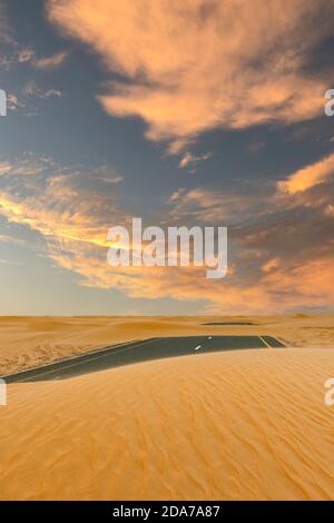 (Selektiver Fokus) atemberaubende Aussicht auf eine verlassene Straße, die von Sanddünen bedeckt ist, die durch die Wüste Dubais laufen. Dubai, Vereinigte Arabische Emirate, (UEA). Stockfoto