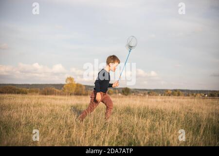 Kleiner Junge mit Schmetterlingsnetz auf der Wiese. Kind spielt Insekten fangen. Sommeraktivitäten für Kinder im Freien. Lernen tierische Fauna Welt ho Stockfoto