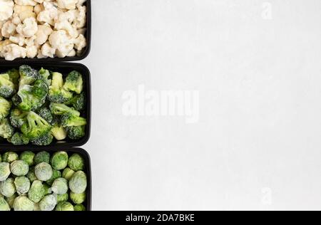 Rand von tiefgefrorenem Gemüse in Behältern auf weißem Hintergrund. Kohl mischen. Rosenkohl, Brokkoli, Blumenkohl. Blick von oben. Speicherplatz kopieren. Stockfoto