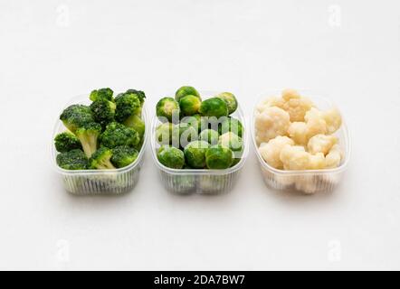 Gefrorenes Gemüse Kohl mischen in Behältern auf weißem Hintergrund. Rosenkohl, Brokkoli, Blumenkohl. Seitenansicht. Stockfoto