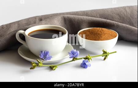 Tasse mit Chicorée Drink, Pulver und blauen Blumen auf weißem Hintergrund. Ein nützlicher Kaffee-Ersatz. Seitenansicht. Stockfoto