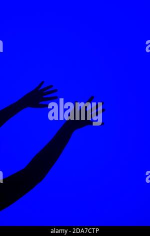 SCHATTEN DER HÄNDE VOR EINEM BLAUEN HINTERGRUND Stockfoto