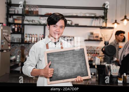 Barista hält eine Tafel und Daumen nach oben auf Stand in Pub vor dem Hotel Stockfoto