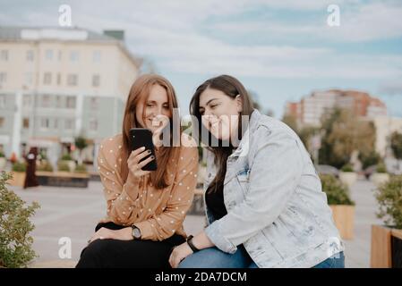 Zwei junge Frauen sitzen in einem Stadtpark mit einem Telefon 1 Stockfoto